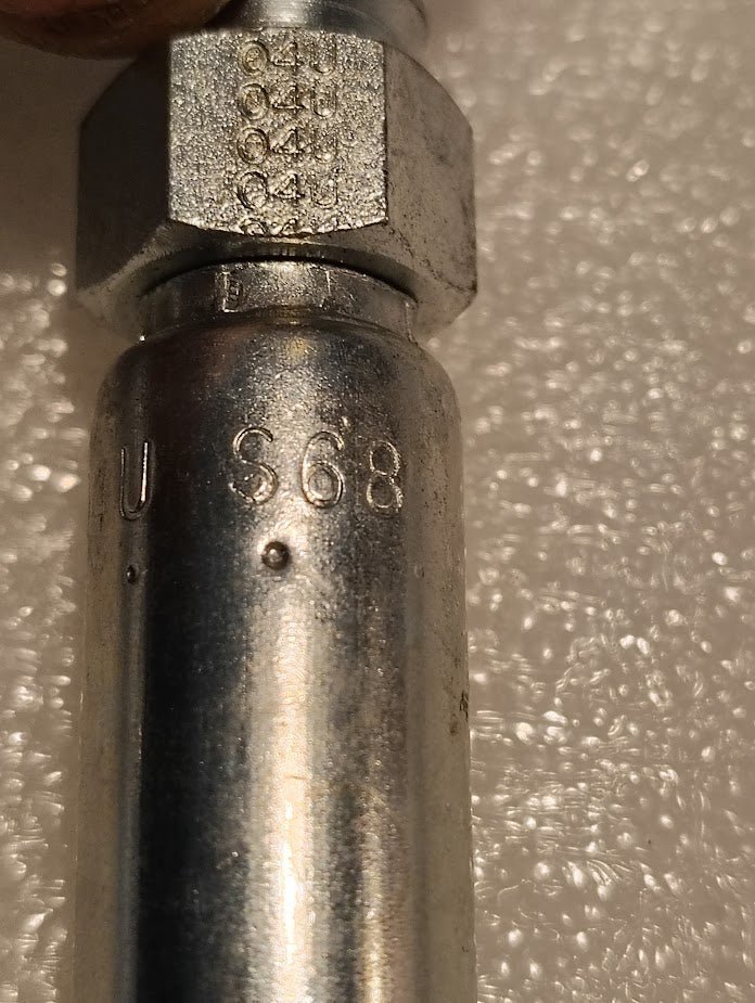 A close-up shows a metal cylinder engraved with 68 U.S. and numbers 0410, 0441, 0455, featuring a shiny surface suggestive of hydraulic hose components. It likely belongs to products like the Weatherhead 04U-S68, a Parker-compatible 1/4 Hose x 1/2 ORF Female Fitting - Straight Swivel.