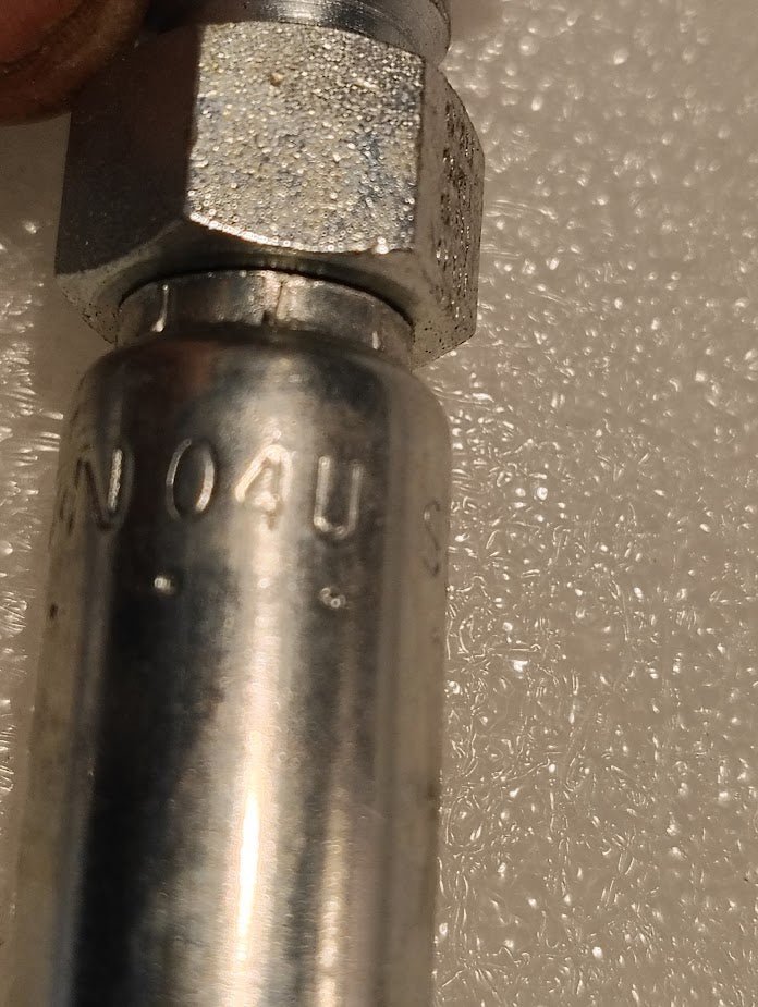 Close-up of a metallic component resembling hydraulic hose fittings, featuring a hexagonal nut and engraved with N 04U S on the cylindrical body. The shiny surface suggests Weatherhead durability. This is the 04U-S68, a Weatherhead 1/4 Hose x 1/2 ORF Female Fitting - Straight Swivel.