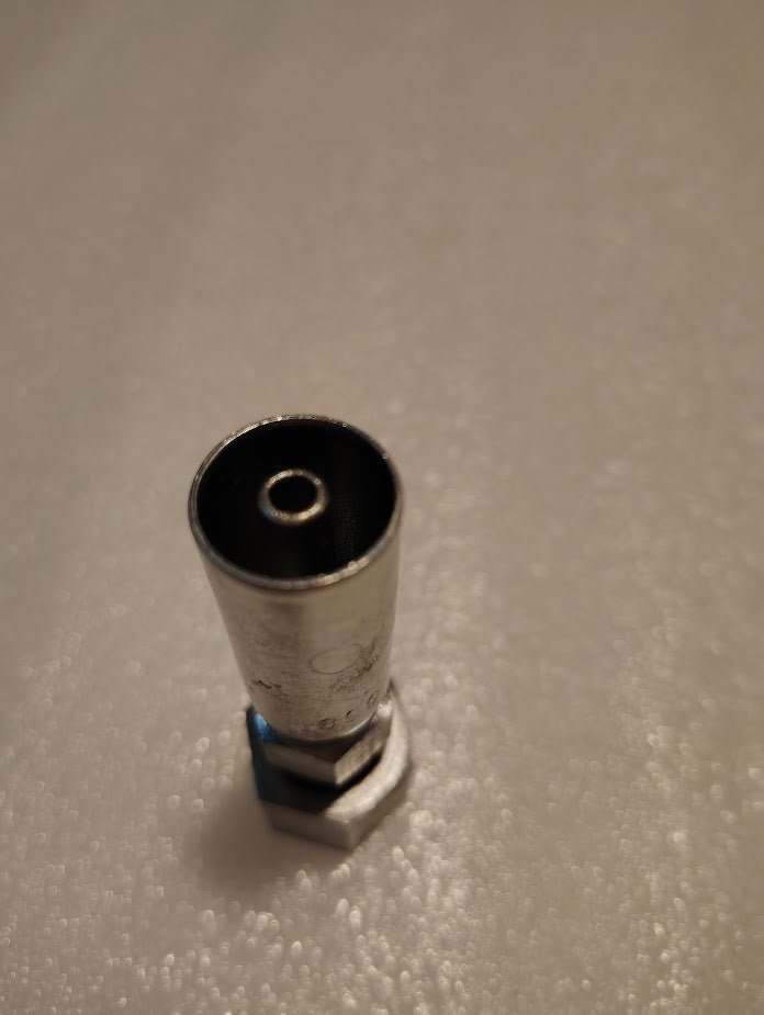 Close-up of a metallic hex socket with a hollow center and hexagonal base, resembling the Weatherhead 04U-S68 1/4 Hose x 1/2 ORF Female Fitting - Straight Swivel, set against a textured light background.