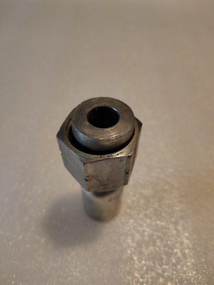 A close-up of the Weatherhead 08U-S72 fitting, a metallic, cylindrical piece with a hexagonal nut at the top, resting on a textured white surface. The aged hydraulic hose fitting shows visible wear.