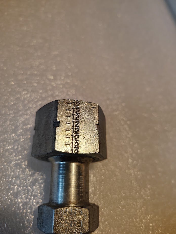 A close-up of the Weatherhead 08U-S72 fitting, used for hydraulic hose connections, showcases engraved numbers 1 to 18 on its hexagonal side. The metal rests gracefully on a textured, light-colored surface.