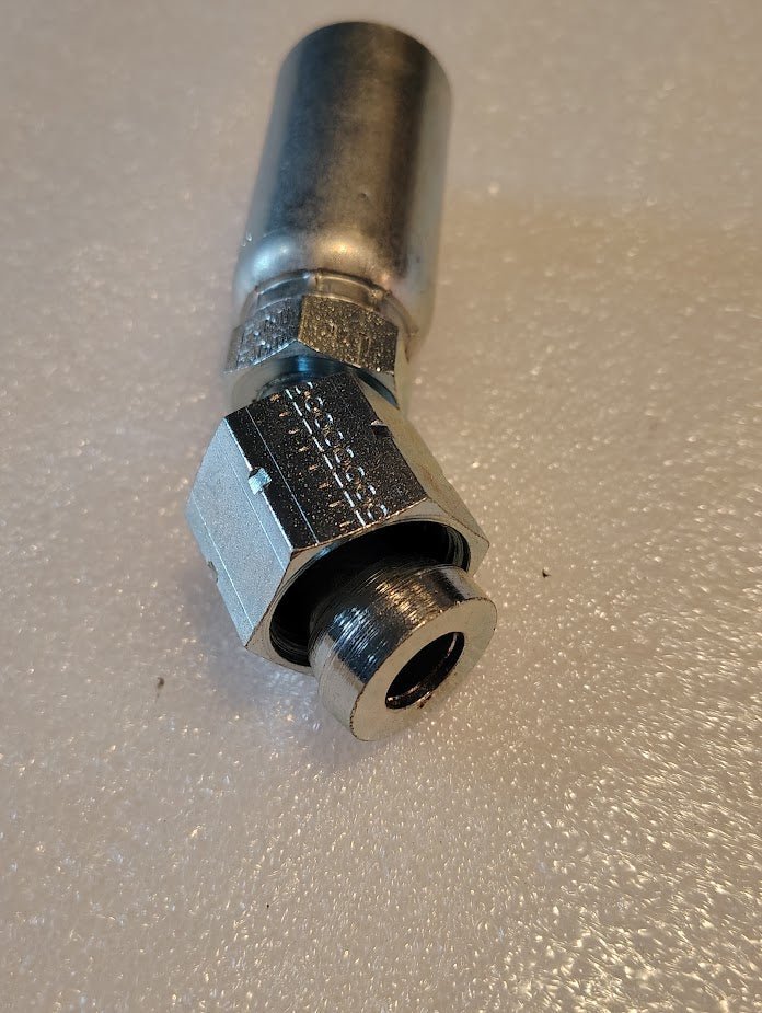 The 10U-L70 Weatherhead fitting, 5/8 Hose x 5/8 ORF Female with a 45 Swivel, sits on a textured white surface. Its metallic design features a threaded end and hexagonal nut, blending shiny and matte finishes to highlight its robust engineering.
