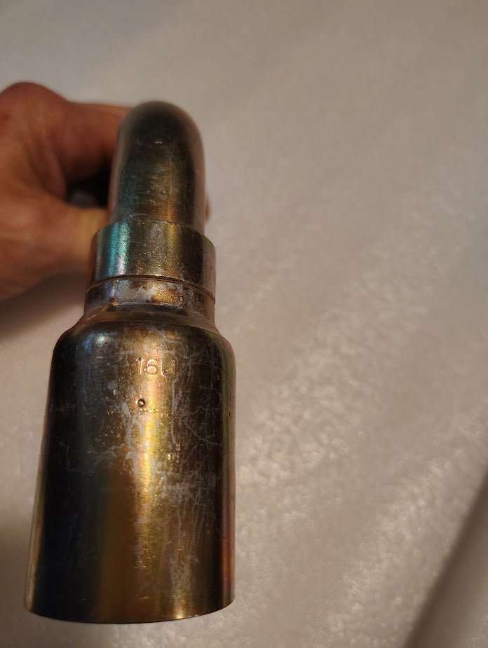A hand holds a slightly tarnished 16U-A76 Weatherhead brass nozzle resembling Parker hydraulic fittings, set against a white background. The fitting shows wear, with 16 visible on its bent tubular shape.