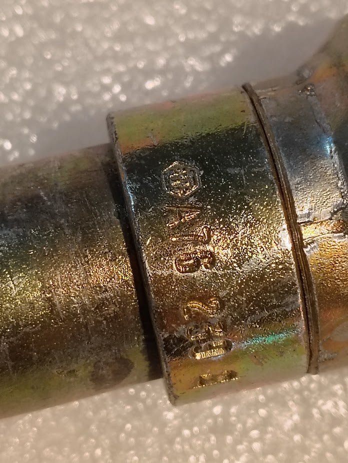 Close-up of a Weatherhead 16U-A76 fitting with markings and a brass metallic finish against a white textured background, showing slight wear and discoloration.