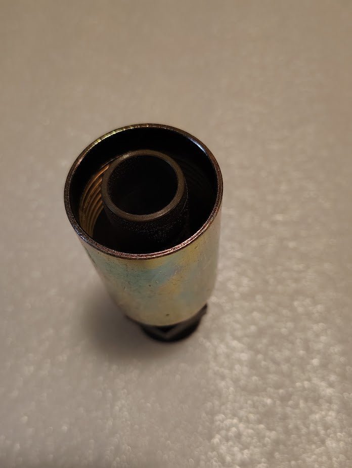 A close-up of a Weatherhead 12U-P62 fitting stands upright on a textured surface. The metallic shell has a slightly tarnished finish, with the interior appearing dark and hollow, suggesting its part of a hydraulic hose system or industrial component.