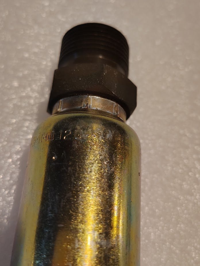 A Weatherhead 3/4 Hose x 3/4 BSPT Male Fitting - Straight Solid, model 12U-P62 with a shiny metallic surface and partially visible engraved text, sits on a textured white surface.