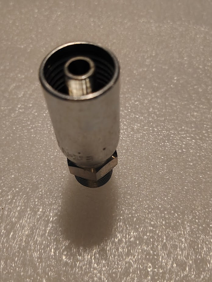The Weatherhead 3/8 Hose x 3/8 BSPT Male Fitting, model 06U-P56, is a shiny metallic cylinder with inner and outer threads and a hexagonal nut at the base, standing upright on a textured white surface.