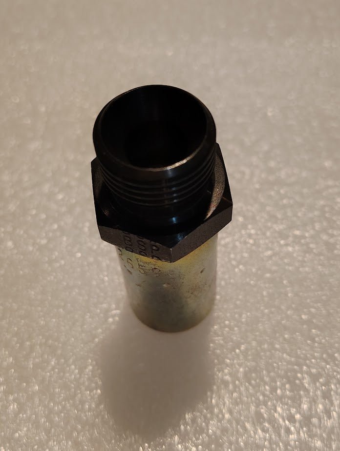 A 06U-P58 Weatherhead fitting (3/8 hose x 1/2 BSPT male), with a metallic cylindrical body and a hexagonal base, stands vertically on a textured white surface, evoking industrial design typical of interchangeable fittings used in hydraulic hoses.