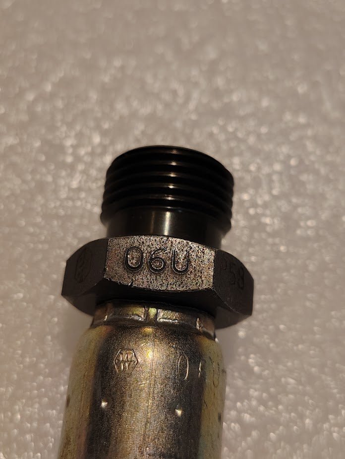 Close-up of a metallic 06U-P58 fitting, displaying engraved 06U and compatible with Weatherhead fittings, on a textured white background.