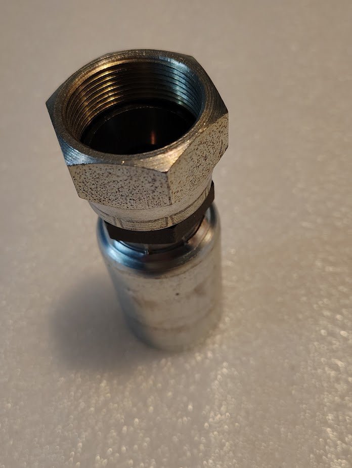 A 12U-30K Weatherhead 3/4 Hose x M30x1.5 Komatsu Female Fitting is vertically positioned on a textured white surface. The metallic fitting, compatible with 100R1 and featuring a hexagonal end and threaded interior, is designed for straight swivel use with Weatherhead fittings.