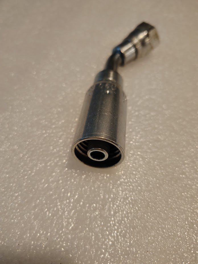 The scene highlights a 06U-10D Weatherhead fitting, showing the circular input end on a textured surface. Its cable, connected to a small component, extends from the M16x1.5 DIN Female Fitting - 45° Swivel. The softly lit background complements its compatibility with Parker fittings.