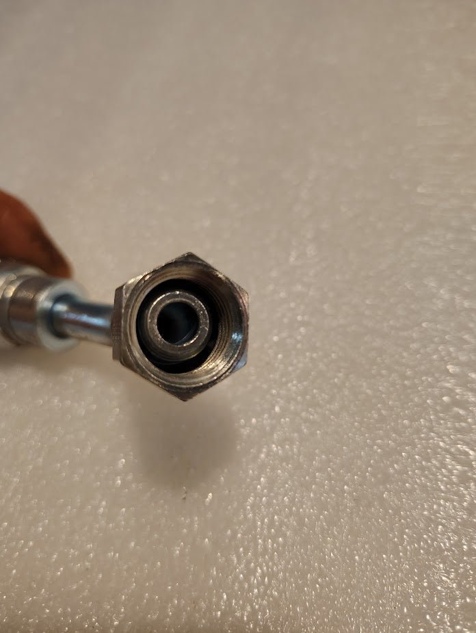 Close-up of a 06U-10D Weatherhead 3/8 Hose x M16x1.5 DIN Female Fitting - 45 Swivel with threaded interior, attached to a metallic pipe on a textured white background, enhancing its industrial appeal.