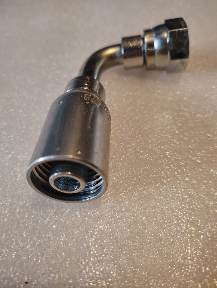 A Weatherhead 08U-65D 1/2 Hose x M22x1.5 DIN Female Fitting rests on a textured light gray surface. Its shiny exterior features ridges, designed for seamless connection with 100R series hoses.