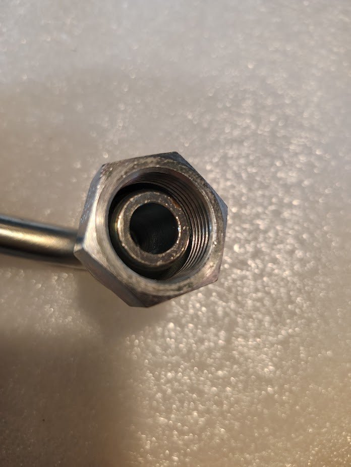 Close-up of an 08U-65D Weatherhead 1/2 Hose x M22x1.5 DIN Female Fitting - 90 Swivel, showcasing its metallic hexagonal nut with threaded interior on a curved tube, against a textured light background.