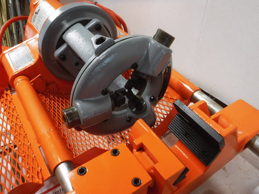 Close-up of a reconditioned Aeroquip FT1013-1-5 Reusable Hose Assembly Machine with an orange frame, quick wrench type chuck, gray threading die head, and black clamps on a metal grid platform.
