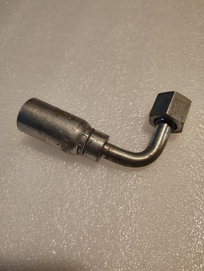 A Weatherhead 3/8 Hose x 3/8 ORF Female Fitting (06U-J36 | CS34-6X6) with a metal bent tube, hex nut, and cylindrical connector lies on a textured light surface; compatible with Weatherhead fittings.