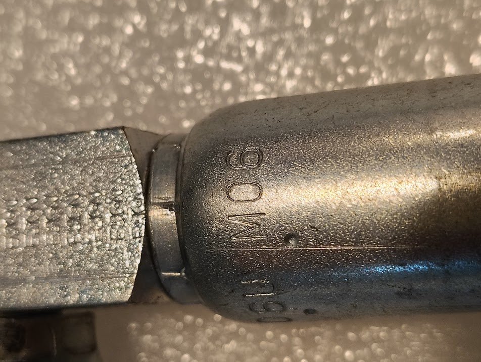 Close-up of a Weatherhead 06U-M06 (3/8 Hose x 3/8 NPTF Male Fitting, CS14-6X6) metallic fitting marked 160 M, resting on a textured white surface; the metal shows slight wear and clear reflections.
