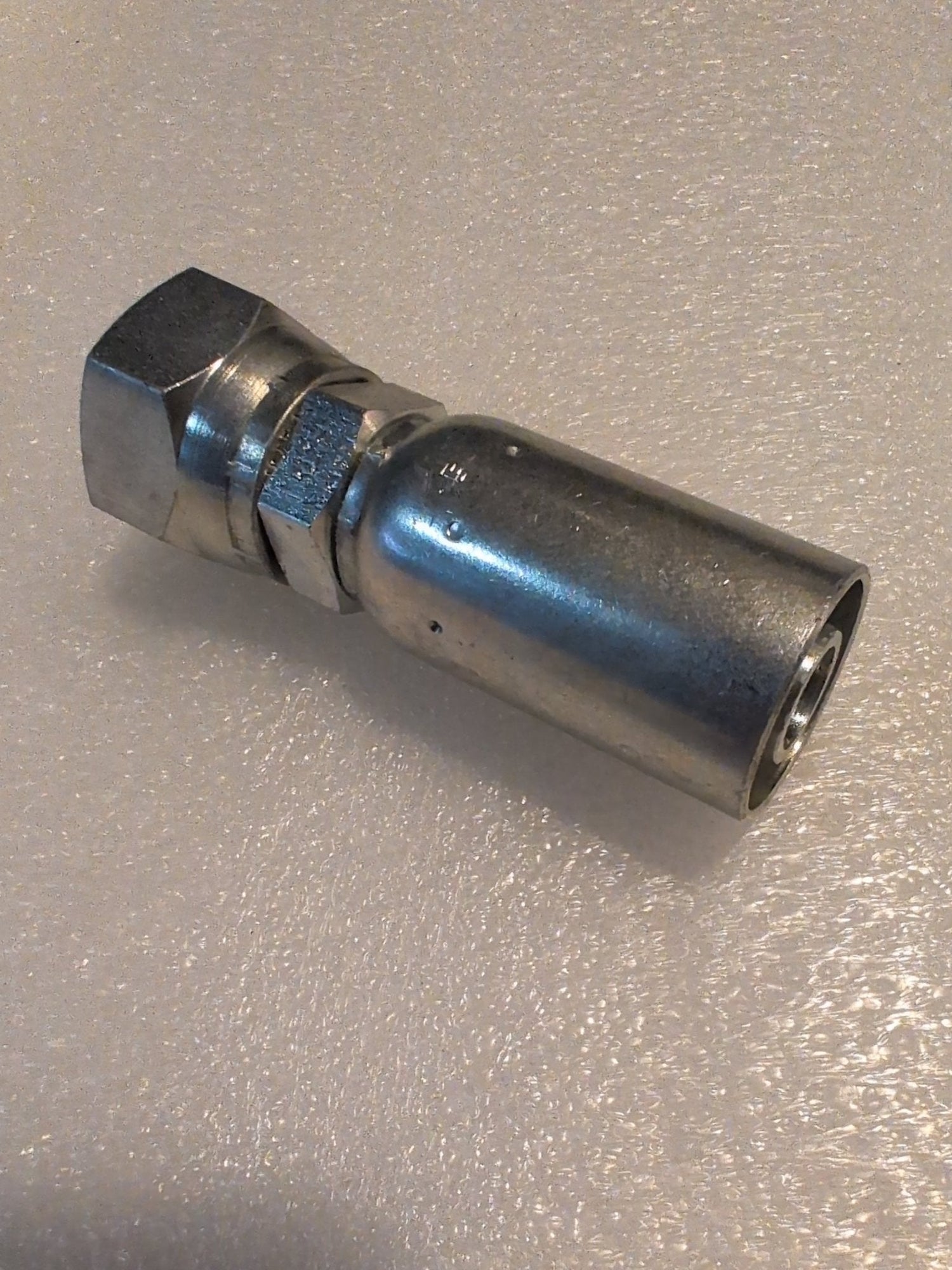 A close-up of a 10U-612 Weatherhead 5/8 Hose x 3/4 JIC Female Fitting (CS09-10X12), similar to those for 100R1 hoses, resting on a textured white surface.
