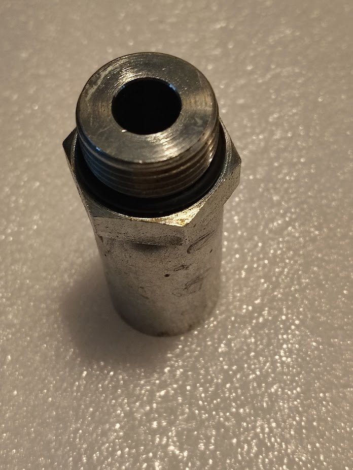 A close-up of the 10U-P12 | Weatherhead 5/8 Hose x 3/4 ORB Male Fitting (CS11-10X12), a metal hexagonal threaded pipe fitting, shown upright on a textured white surface.
