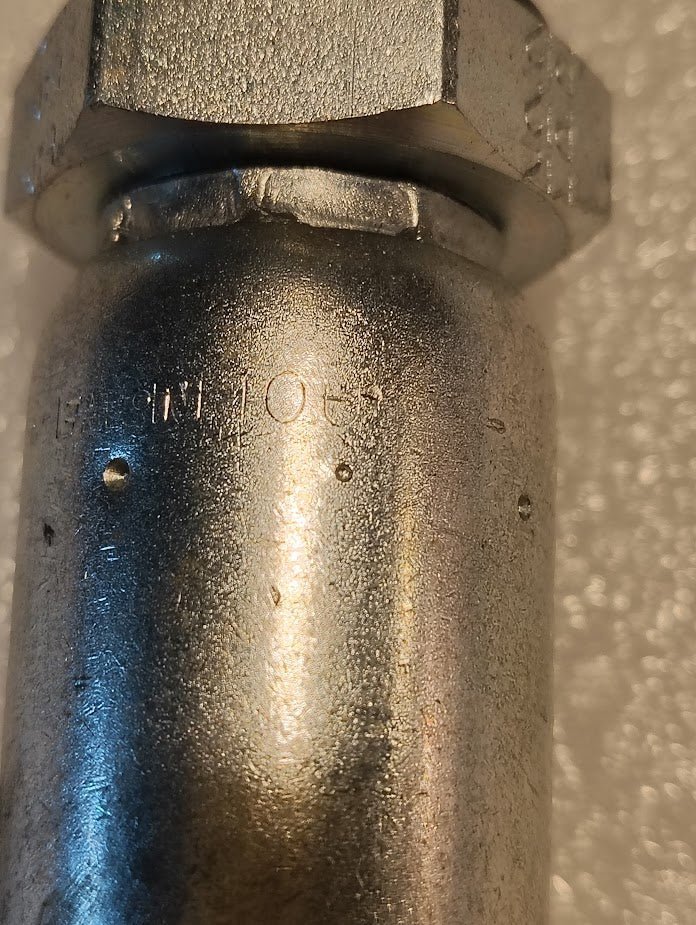 A close-up of the 10U-P12 | Weatherhead 5/8 Hose x 3/4 ORB Male Fitting (CS11-10X12) shows its metallic, cylindrical body with a hexagonal nut, reflective textured surface, faint engraved numbers, and a light-colored background.