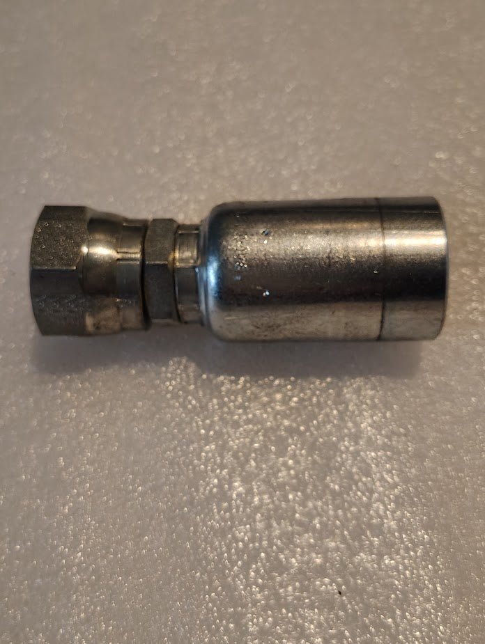 A close-up image of the Weatherhead 12U-12L 3/4 Hose x 3/4 JIS Female Fitting (CS40-12X12), a metal hydraulic quick-connect, shown horizontally on a textured, light-colored surface.