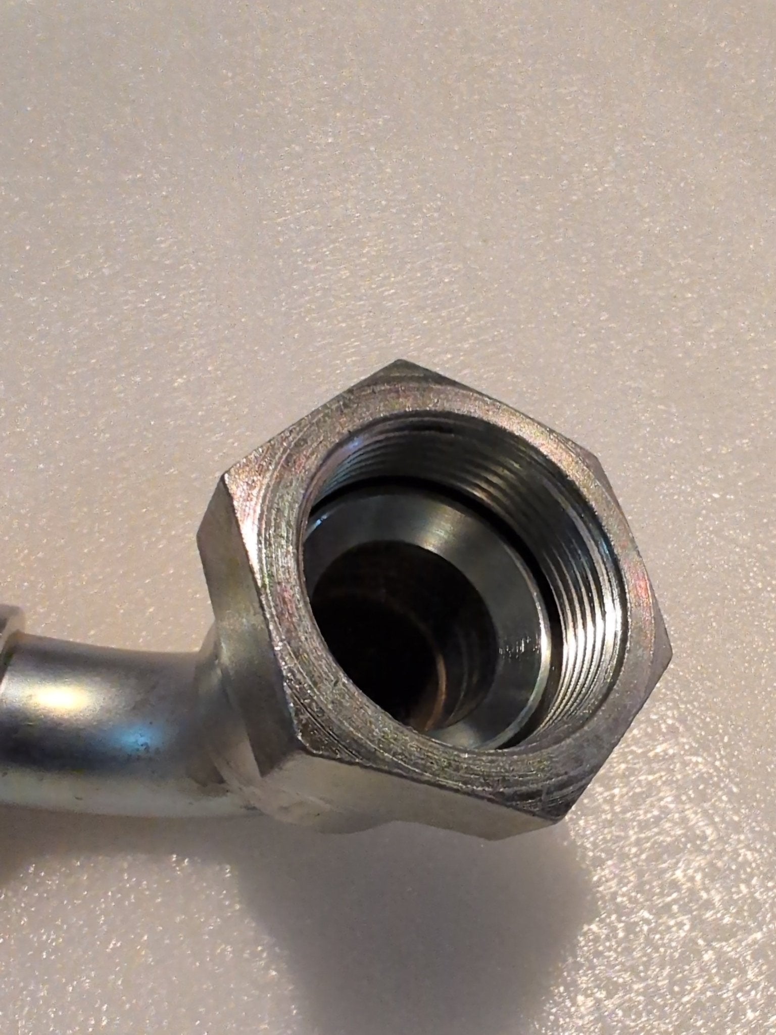 Close-up of a 20U-677 Weatherhead 1 1/4 Hose x 1 1/4 JIC Female Fitting (CS26-20X20), featuring a hexagonal nut and threaded interior, shown on a textured, light-colored surface.
