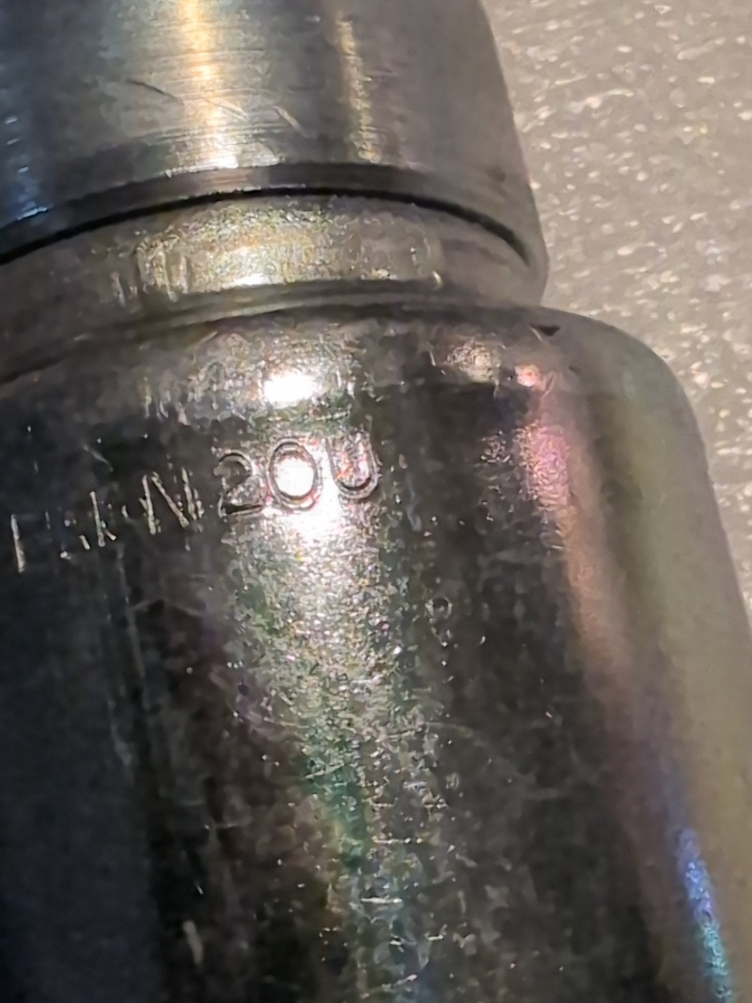 Close-up of a Weatherhead 20U-677 fitting (1 1/4 hose x 1 1/4 JIC female, CS26-20X20) with 20U engraved on its shiny, slightly reflective metallic surface. Textured marks highlight the durable finish.