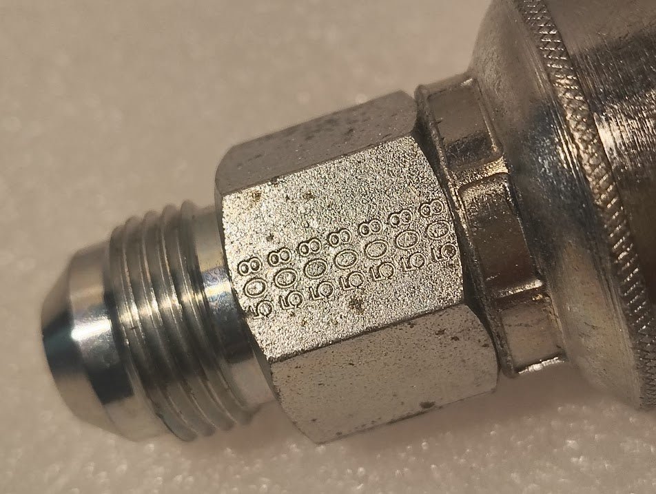 Close-up of a 43008U-508 | 1/2 Hose x 1/2 JIC Solid Fitting - Straight (GW08-8x8) attached to a larger metallic component, resting on a textured light surface.