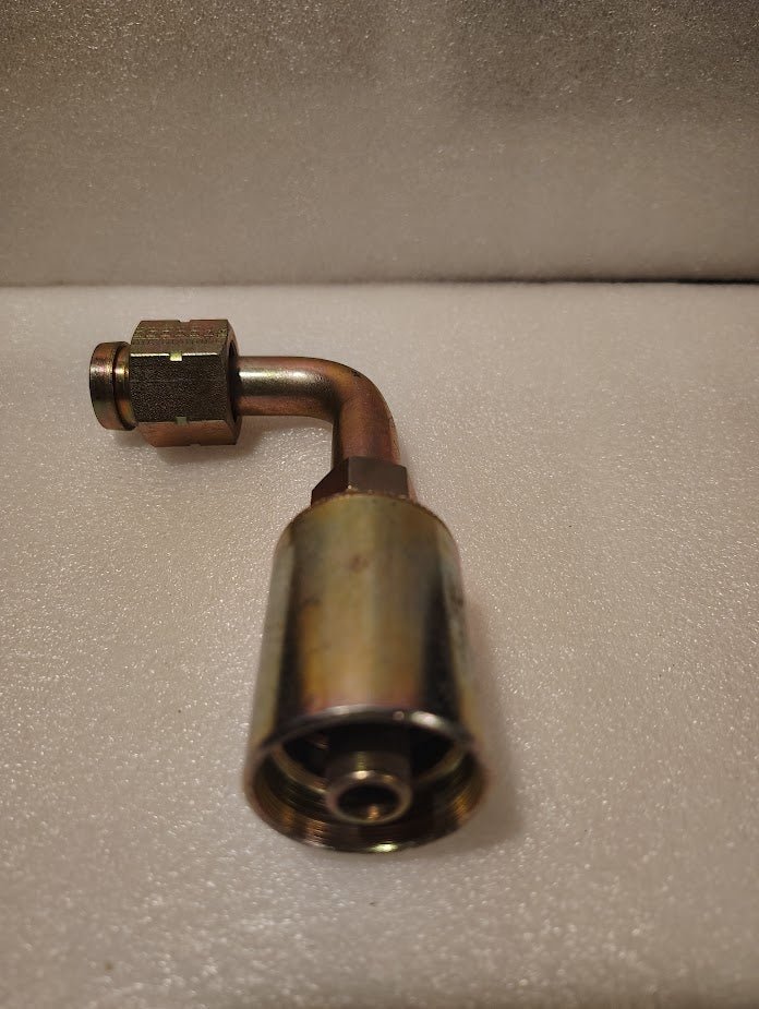A 43008U-A70 | 1/2 Hose x 5/8 ORFS Swivel Fitting - 90 Long Bend (GW33-8x10) lies on a textured white surface, showing its brass build with a threaded female end and compression fitting.