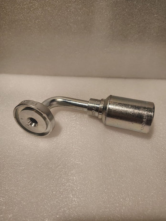 A close-up of the 43008U-G76 | 1/2 Hose x 1 Code 61 Flange Fitting - 90 bend (GW53-8x16), resembling a metal socket wrench adapter, resting on a soft white surface with flange and hose ends visible.