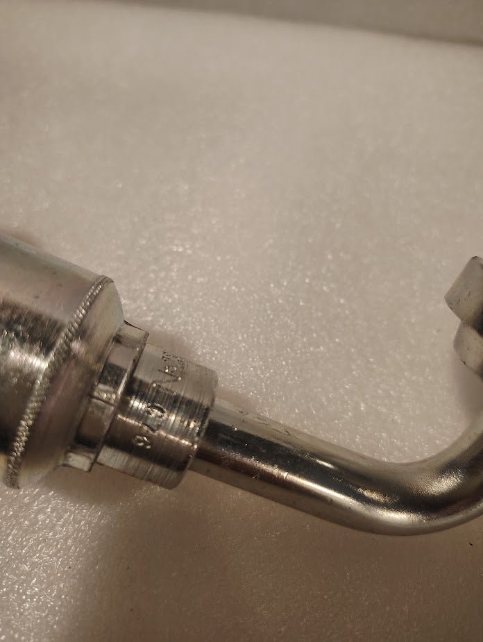 A close-up of the 43008U-G76 | 1/2 Hose x 1 Code 61 Flange Fitting - 90 bend (GW53-8x16), a shiny hydraulic fitting with a right-angle bend, resting on a soft white surface.