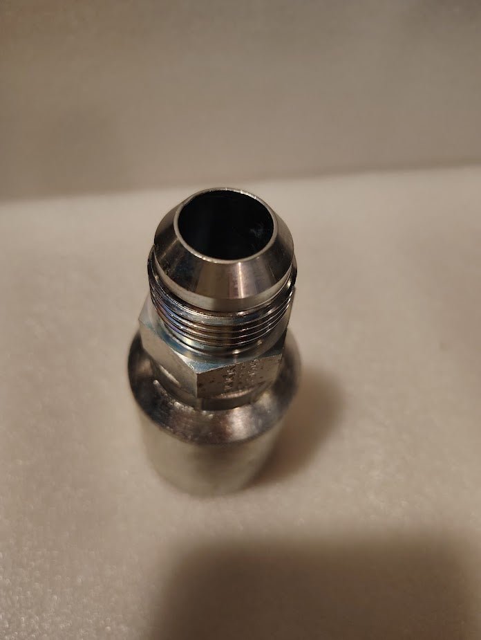 A close-up photo of a Weatherhead 43012U-512 3/4 Hose x 3/4 JIC Male fitting (GW08-12x12), with threading and a beveled edge, placed upright on a soft, white textured surface.