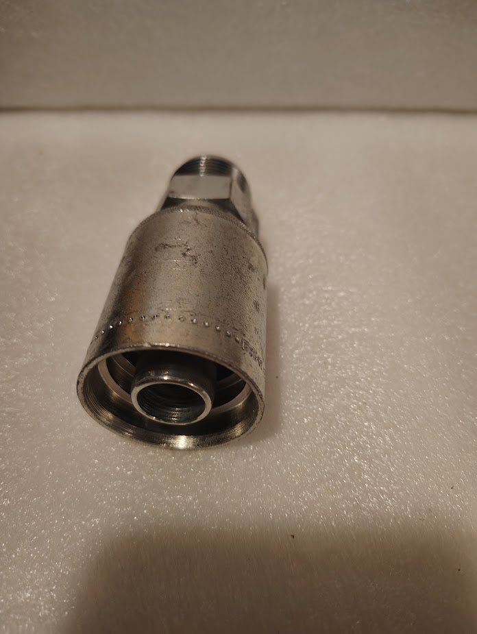 A close-up of a 43012U-514 | 3/4 Hose x 7/8 JIC Solid Fitting - Straight (GW08-12x14) on a white textured surface, with the threaded end facing the camera.