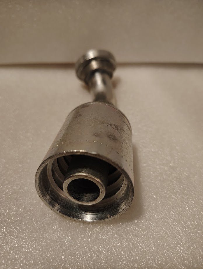 Close-up of a Weatherhead 43012U-G42 GW50-12x12 fitting, 3/4 hose x 3/4 Code 61 flange, featuring metallic threads and rings, placed on a textured white surface; used with compatible hoses in mechanical or plumbing systems.