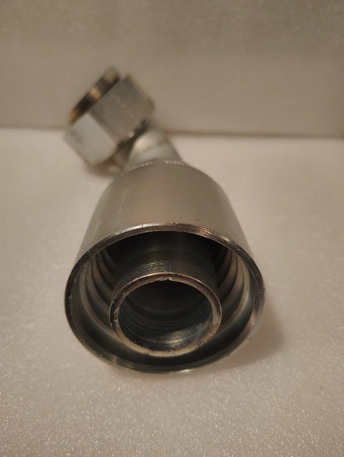 Close-up of a 43024U-A44 | 1 1/2 Hose x 1 1/2 ORFS Swivel Fitting - 90 Short Bend (GW32-24x24), showing interior threading, on a white textured surface.