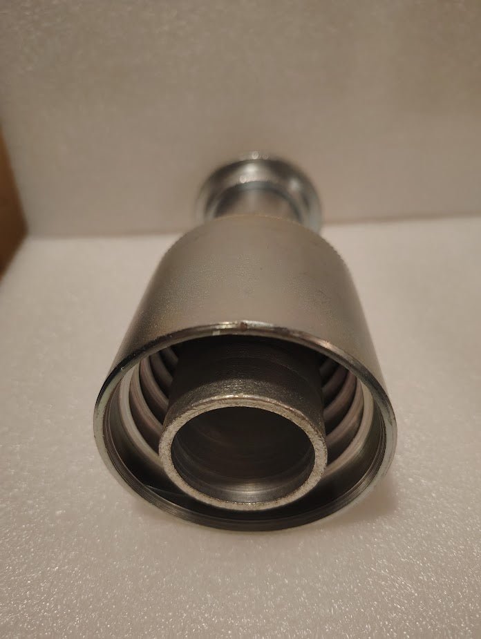 A close-up photo of the 43024U-G24 | 1 1/2 Hose x 1 1/2 Code 61 Flange Fitting (Straight), showing its metallic cylindrical body with inner coil spring and round openings, placed on a white textured surface.