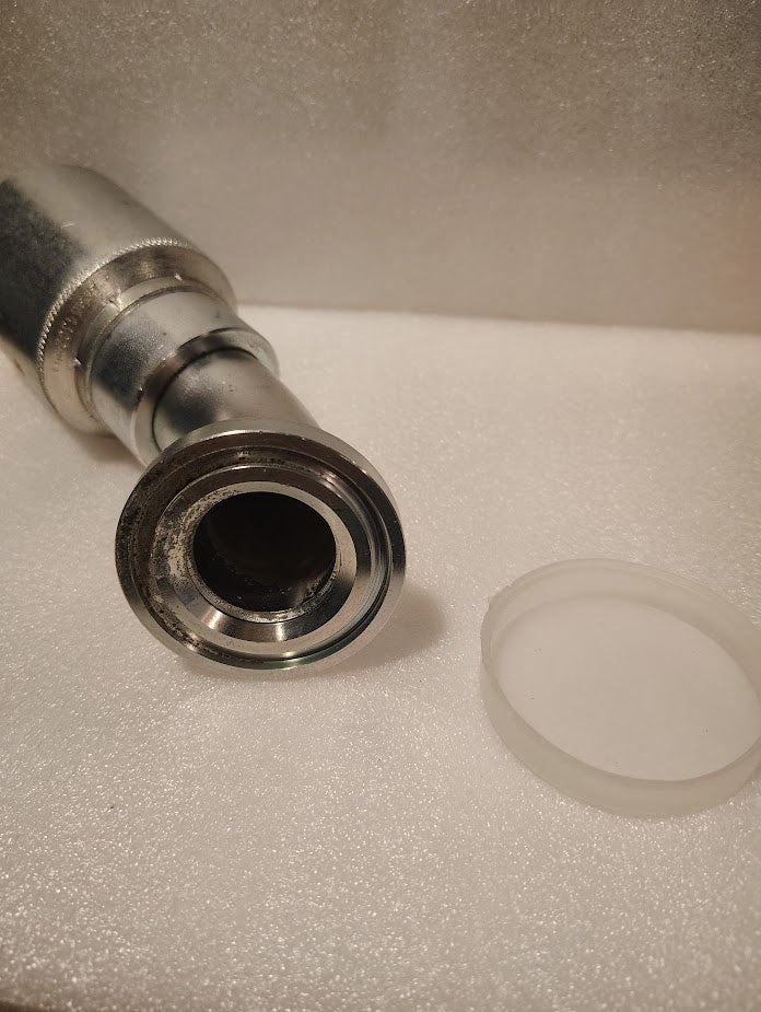 A close-up of the 43024U-G54 | 1 1/2 Hose x 1 1/2 Code 61 Flange Fitting - 45 bend (GW50-24x24) with a circular opening, lying on a white textured surface beside a translucent plastic cap.