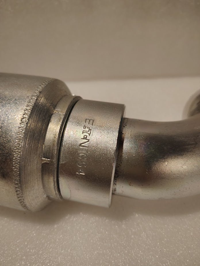Close-up of a 43024U-G54 1 1/2 Hose x 1 1/2 Code 61 Flange Fitting with a 45° bend (GW50-24x24), displaying its metallic, textured finish and engraved markings against a soft, light background.