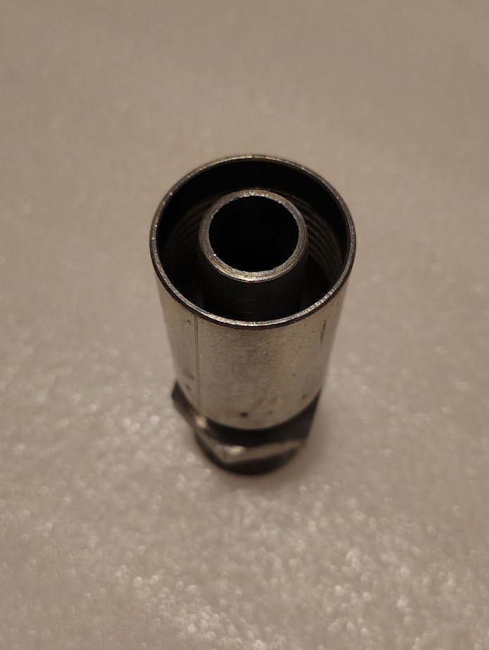 The close-up reveals the 12U-116 Weatherhead fitting, a cylindrical metal object with threaded inner and outer surfaces. Its dark interior contrasts with its smooth, reflective exterior, suggesting it forms part of a larger mechanical assembly.