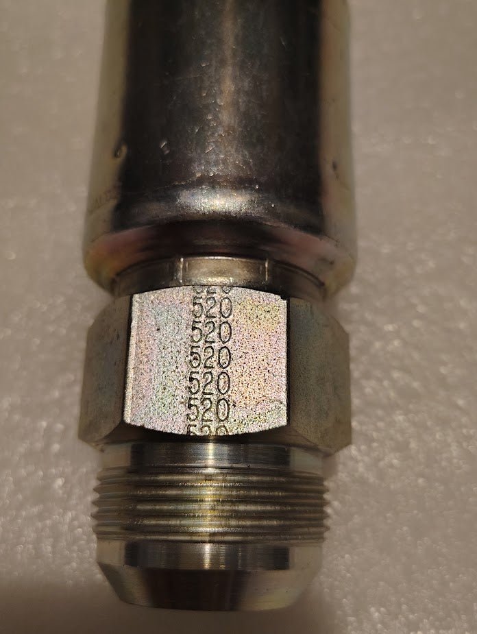 A close-up of a 20U-520 Weatherhead 1 1/4 Hose x 1 1/4 JIC Male Fitting shows the metallic pipe connector with threading and a hexagonal nut, etched with 5520 along the facet. The background features a textured light surface similar to those used for settings with 100R1 hoses.