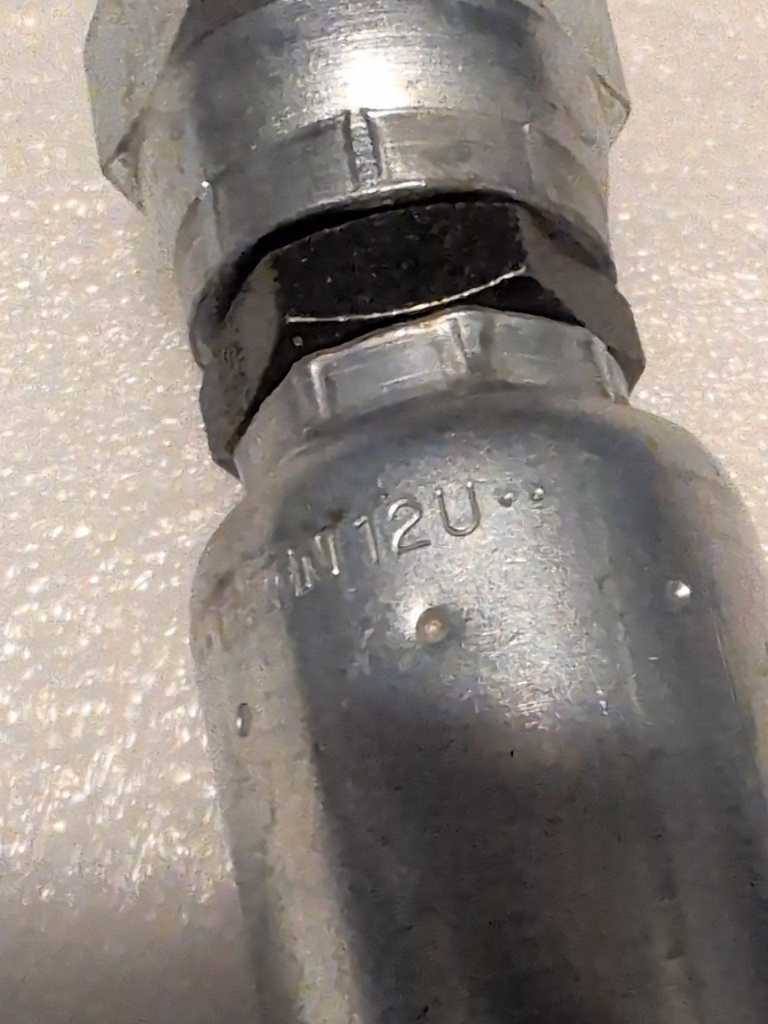 Close-up of a metallic pipe fitting against a textured surface, featuring a hexagonal nut with 12U-362 marking, indicating compatibility with 100R1 hydraulic hoses. Its the Weatherhead 3/4 Hose x 3/4 BSPP Female Fitting - Straight Swivel.