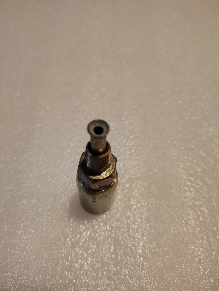 The 06U-B04 Weatherhead 3/8 Hose x 1/4 Inverted Male Fitting, resembling Parker hydraulic fittings, stands upright on a textured white surface. It has a cylindrical shape with a narrow opening at the top.