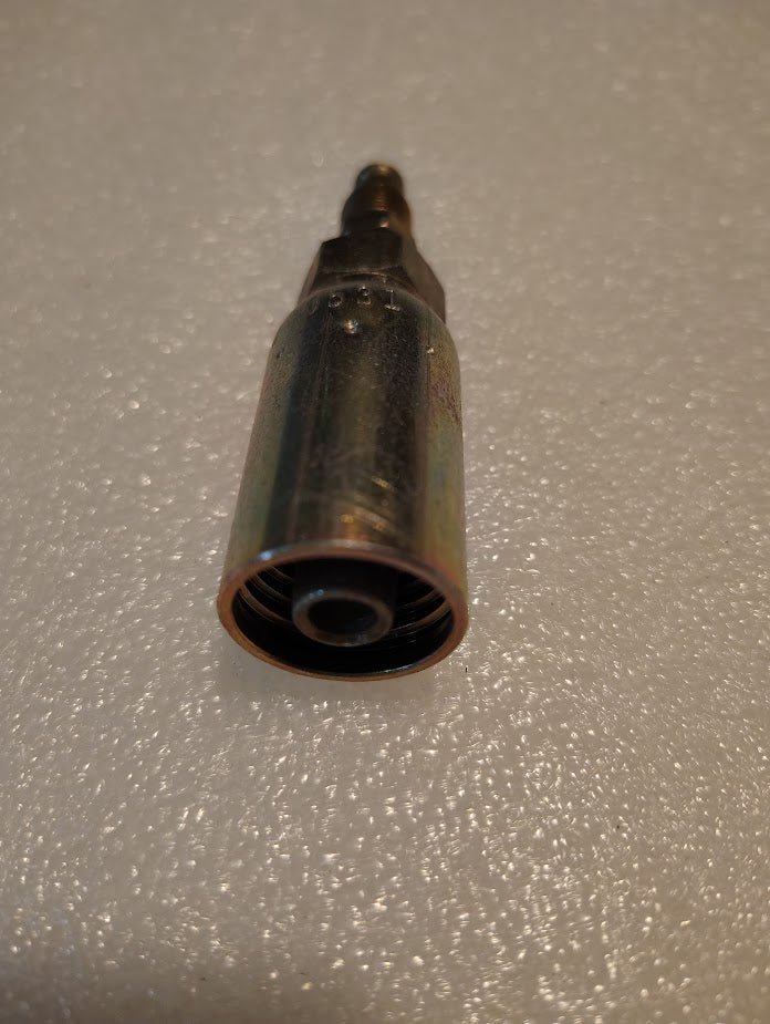 A close-up of the 06U-B04 Weatherhead fitting shows its metal quick-connect design on a white surface, with a threaded interior and narrow neck perfect for 100R1 compatible hydraulic hose fittings.