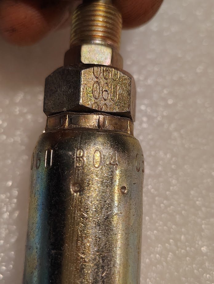 A close-up of a metallic hexagonal bolt engraved with 06U B04 shows a partially threaded connection to a cylindrical metal part. Compatible with 100R1 hydraulic hose fittings, its the Weatherhead 06U-B04, a 3/8 Hose x 1/4 Inverted Male Fitting - Straight Swivel, set against a textured white background.