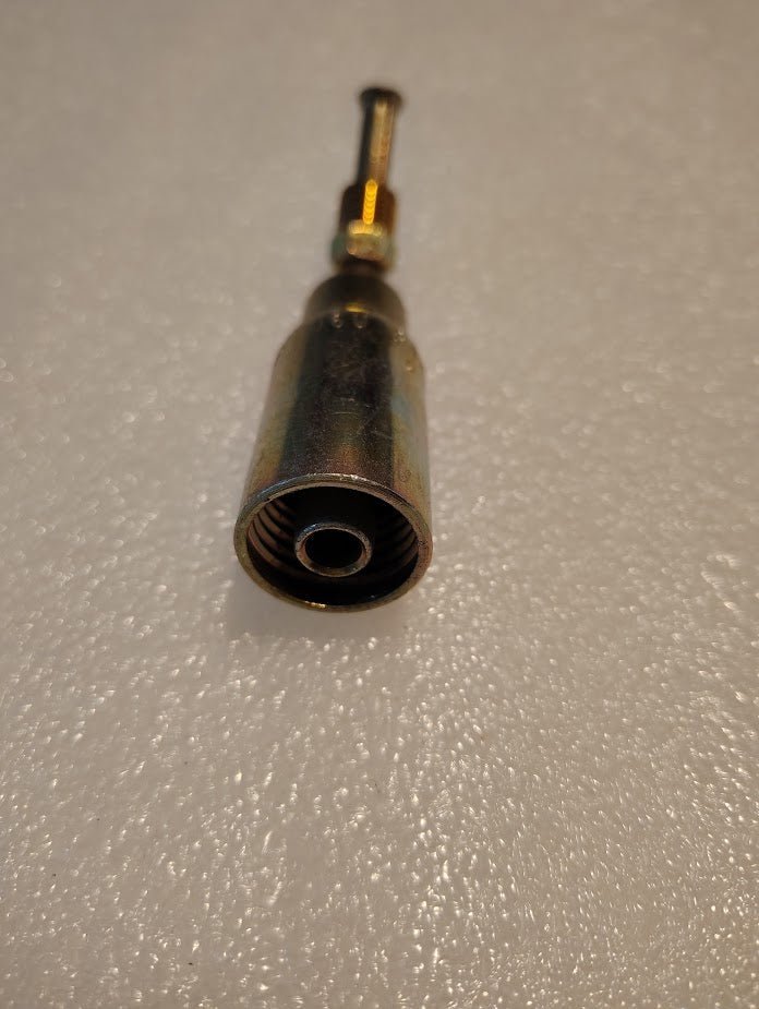 Close-up of 06U-B44 Weatherhead 3/8 Hose x 1/4 Inverted Male Fitting-45 Swivel, a metallic cylindrical tool with a narrow extension, on a textured surface.