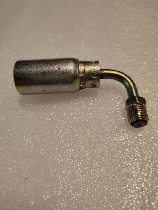 The 06U-B64, a steel Weatherhead 3/8 hose x 1/4 inverted male fitting - 90 swivel, rests on a textured white surface. This metallic, L-shaped pipe fitting shows signs of wear and is potentially compatible with 100R1 for hydraulic hose applications.
