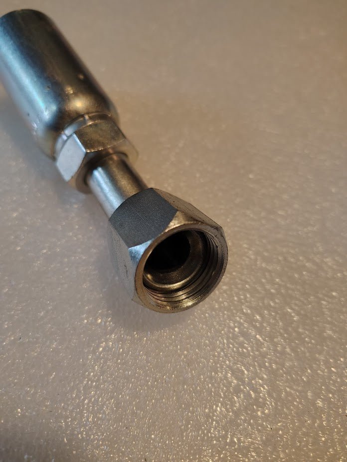 Close-up of a shiny 10U-690 stainless steel hydraulic hose fitting with a hexagonal nut and threaded end on a textured surface. Its reflective finish suggests high quality, compatible with Weatherhead 5/8 Hose x 5/8 JIC/SAE Female Fittings for seamless system integration.