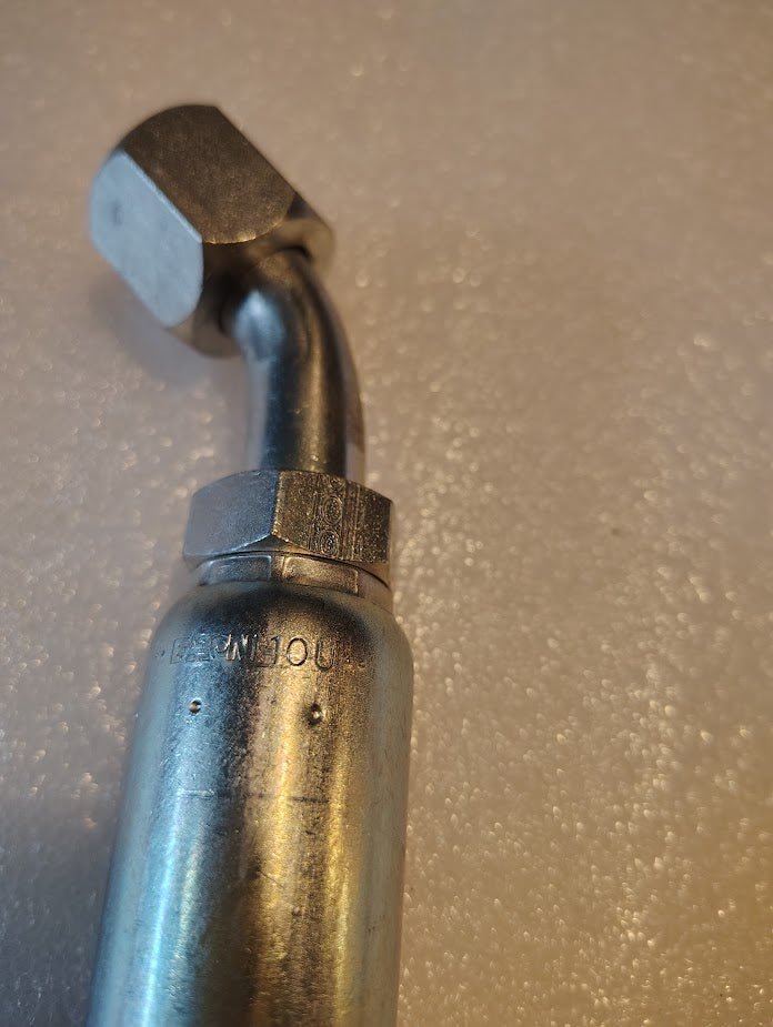Close-up of a Weatherhead 10U-690, a 5/8 Hose x 5/8 JIC/SAE Female Fitting - 45 Swivel, on a textured white surface. It has a hexagonal nut and curved section with faint numbers and letters visible.