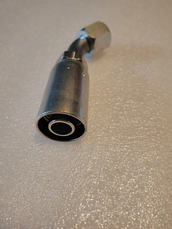 A metal 10U-690 Weatherhead 5/8 Hose x 5/8 JIC/SAE Female Fitting - 45 Swivel with a cylindrical shape and hexagonal end rests on a textured, light-colored surface. Its shiny finish reflects the precision and quality of Weatherhead fittings.