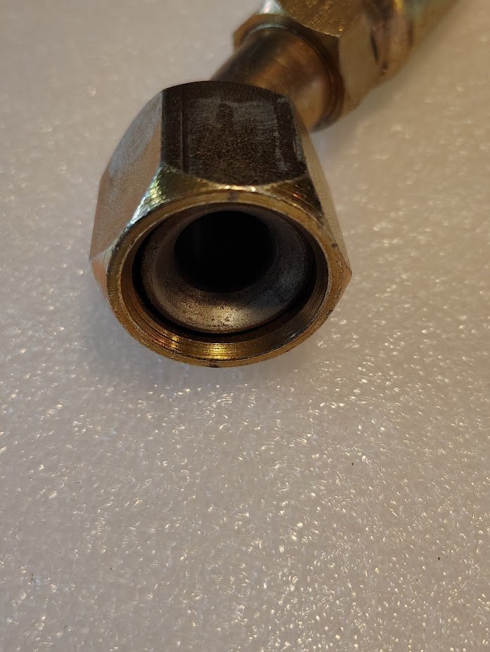 Close-up of a 10U-692 Weatherhead fitting on a textured, white surface. The 5/8 hose x 3/4 JIC/SAE female fitting with a hexagonal nut and cylindrical opening, displays metallic shine and tarnish.